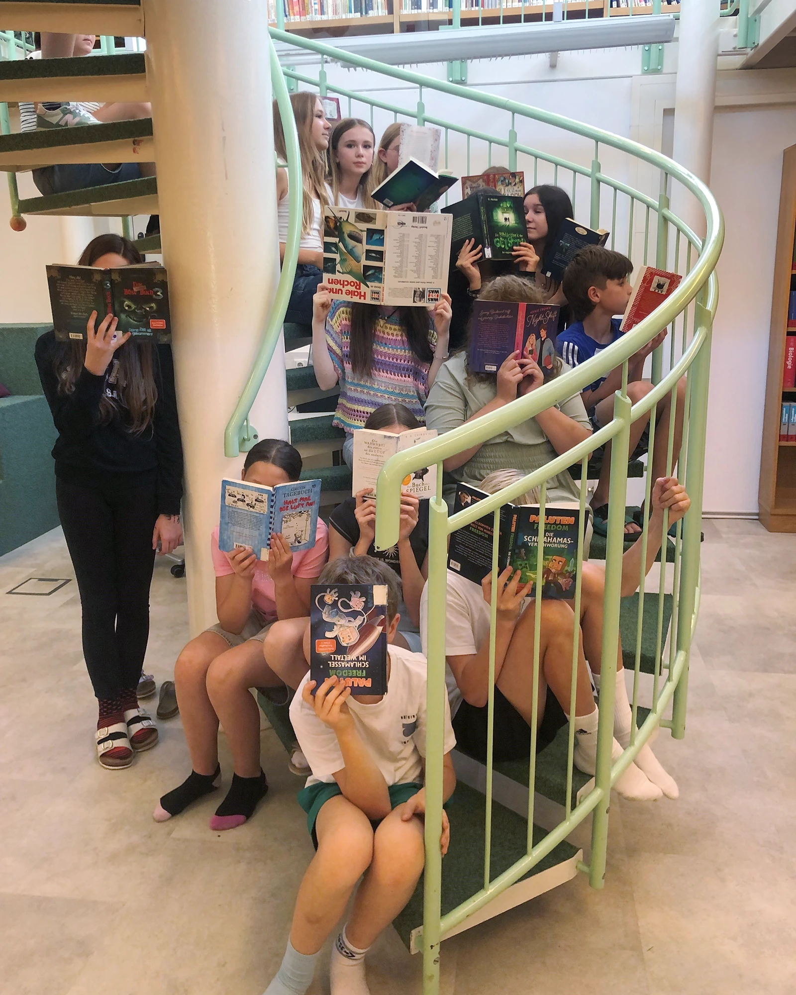 Schülerinnen halten Bücher auf Treppe in Bibliothek